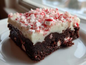 A close-up of a fudgy peppermint brownies square topped with white frosting and crushed candy canes.