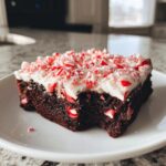 A fudgy square of peppermint brownies topped with white frosting and crushed candy canes.