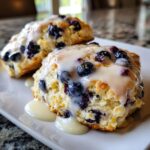 Close-up of two flaky blueberry scones topped with thick, dripping vanilla glaze.