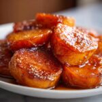 A close-up of several thick slices of candied sweet potatoes glistening with a rich, dark brown glaze.