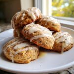 A stack of freshly baked eggnog cookies drizzled generously with white glaze, sitting on a white plate.