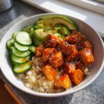 Close-up of delicious salmon bowls featuring glazed salmon cubes over rice with sliced avocado and cucumber.