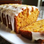 Close-up of a moist sweet potato pound cake loaf with thick white glaze dripping down the sides and a slice cut.
