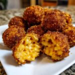 Close-up of golden brown fried mac and cheese balls, one is broken open showing the gooey cheese center.