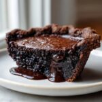 Close-up of a rich, dark slice of hot fudge pie with molten chocolate oozing down the side.