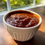 Close-up of thick, rich, dark red homemade bbq sauce served in a small white fluted ramekin.