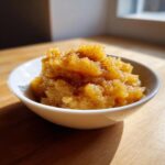 A close-up of chunky, golden homemade applesauce topped with cinnamon, served in a small white bowl.