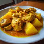 Close-up of tender Jamaican curry chicken pieces served with large chunks of yellow potato in a rich, orange curry sauce.