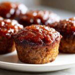 Close-up of a single, perfectly baked mini meatloaf topped with a shiny, thick brown glaze.