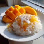 A serving of mango sticky rice topped with sweet coconut cream and sesame seeds.
