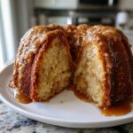 A moist apple dapple cake, cut in half, revealing the interior and covered in thick caramel sauce.