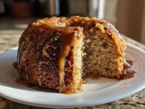 A moist apple dapple cake, shaped like a small bundt, covered in thick caramel sauce with a slice removed.