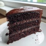 Close-up of a rich, three-layer slice of chocolate cake recipe with glossy dark frosting.