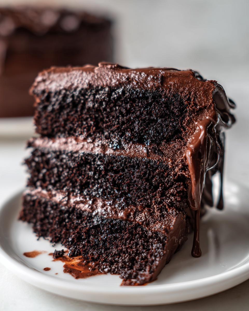 Close-up of a moist, three-layer slice of dark chocolate cake recipe with rich chocolate frosting and dripping ganache.