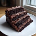 A tall, moist slice of dark chocolate cake with three layers and rich chocolate frosting.