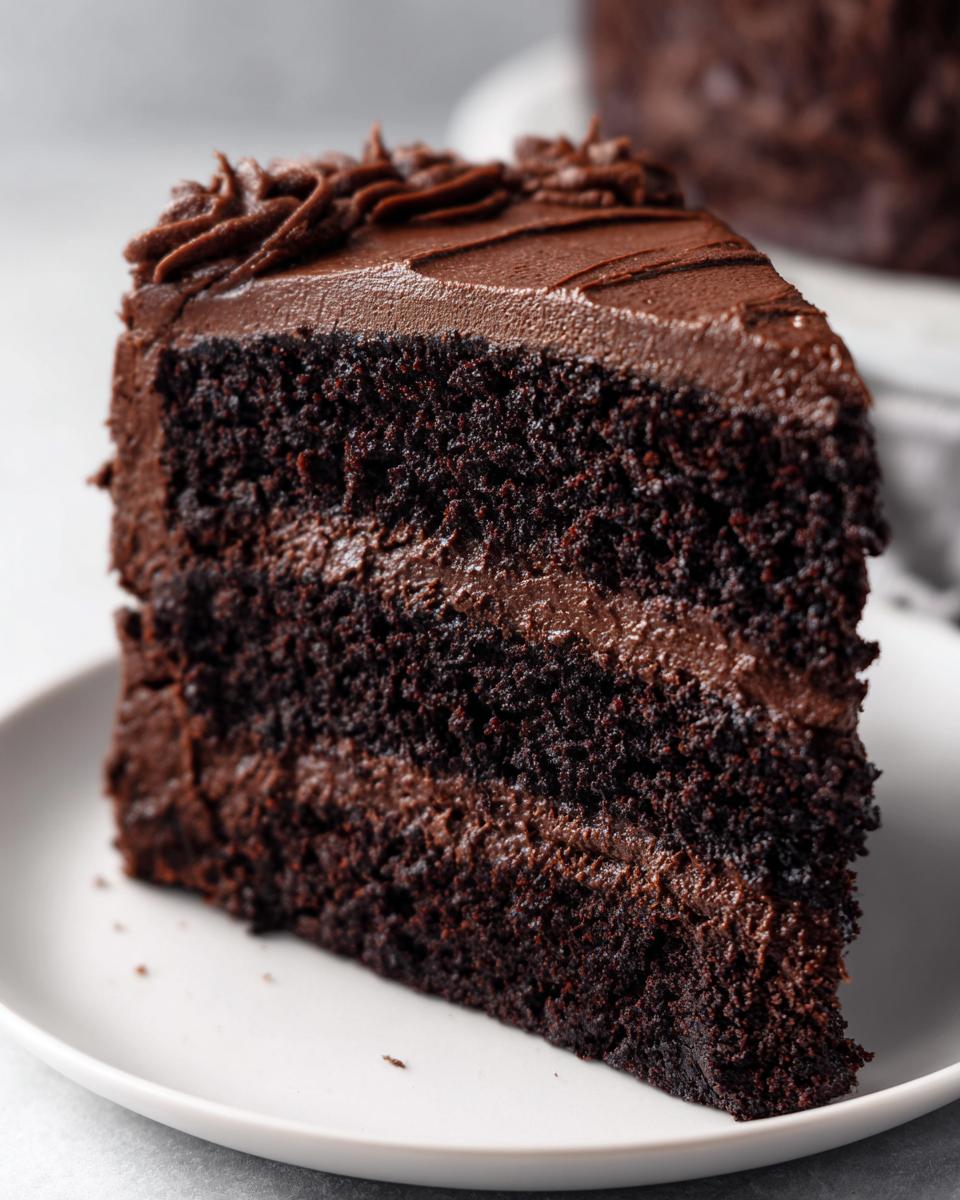 Close-up of a rich, moist slice of three-layer chocolate cake with thick chocolate frosting.