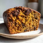 A close-up view of a freshly baked, moist chocolate chip pumpkin bread loaf slice on a ceramic plate.
