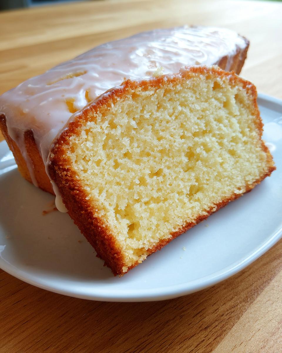 Close-up of a moist slice of cream cheese pound cake showing its dense crumb and golden crust, topped with white glaze.