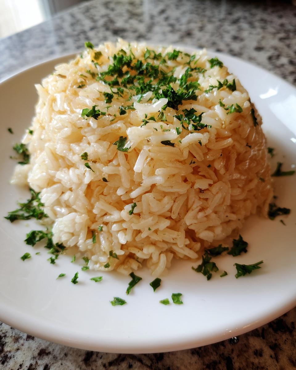 A mound of glistening garlic butter rice topped with fresh chopped parsley, served on a white plate.