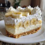 A perfect slice of no-bake banana cream cheesecake with a graham cracker crust, creamy filling, and whipped cream topping with banana slices.
