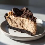 A thick slice of no-bake peanut butter pie with a dark chocolate crust, topped with crushed Oreos.