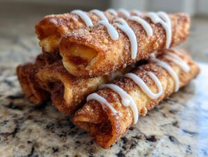 A stack of golden brown peach cobbler egg rolls coated in cinnamon sugar and drizzled with white icing.