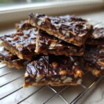 Close-up of stacked squares of rich pecan pie bark with a thick chocolate topping cooling on a wire rack.