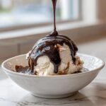A scoop of vanilla ice cream being drenched in rich, glossy chocolate sauce recipe.