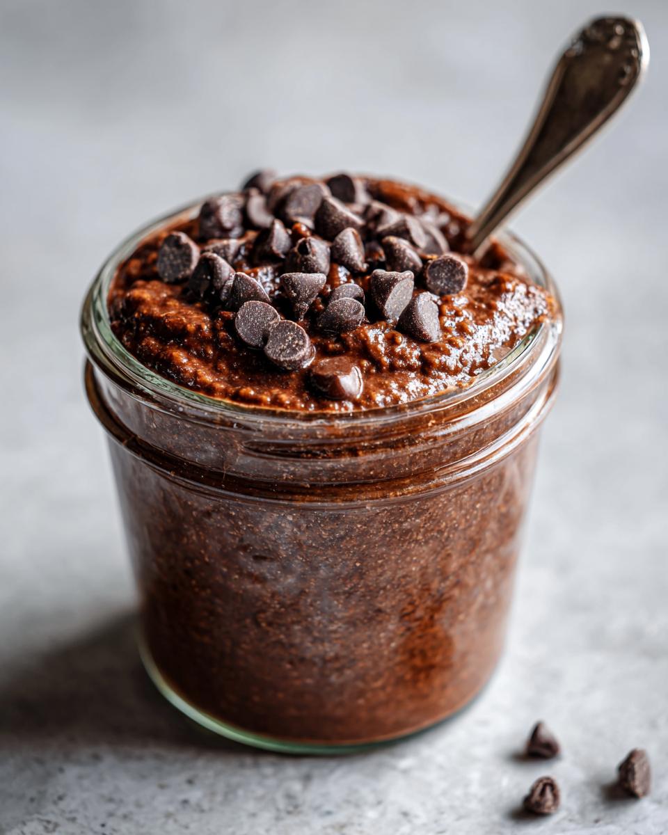 Close-up of rich chocolate overnight oats in a glass jar, topped generously with chocolate chips.