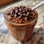 Close-up of rich chocolate overnight oats in a glass jar, generously topped with chocolate chips.