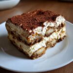 A rich, layered slice of tiramisu recipe dessert dusted heavily with cocoa powder.
