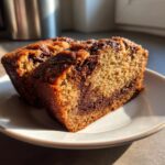 Two thick slices of moist peanut butter banana bread with a rich chocolate swirl, served on a white plate.