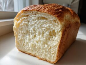 A loaf of freshly baked milk bread, showing its incredibly soft, white crumb texture and golden-brown crust.