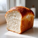 A freshly baked loaf of milk bread, cut to show its incredibly soft, white, and fluffy interior crumb.