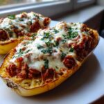 Two halves of spaghetti squash lasagna stuffed with meat sauce and melted mozzarella, topped with parsley.