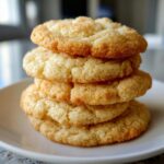 A close-up stack of four golden brown, slightly crinkled sugar cookies dusted with sparkling sugar.