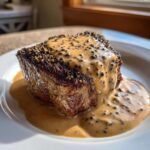 A perfectly seared steak generously topped with creamy peppercorn sauce and whole peppercorns.