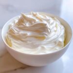 A white bowl filled with perfectly smooth and stiff royal icing recipe mixture, ready for decorating.