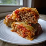Close-up of two delicious cabbage rolls cut in half showing the savory filling of ground meat and rice, covered in tomato sauce.