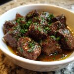 Close-up of tender crockpot steak bites coated in a savory sauce and topped with fresh parsley.