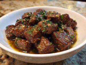 Close-up of tender crockpot steak bites coated in a rich, buttery sauce and topped with fresh parsley.