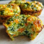 A close-up of a savory vegetable egg muffin with spinach and carrots, showing a bite taken out, revealing the fluffy interior.