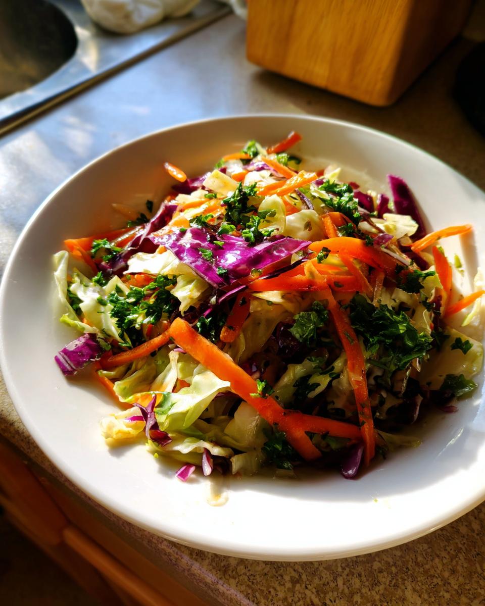 A bright white bowl filled with colorful cabbage salad featuring shredded green cabbage, purple cabbage, carrots, and fresh parsley.