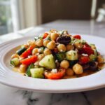 Close-up of a fresh mediterranean chickpea salad featuring chickpeas, cucumbers, tomatoes, olives, and feta.