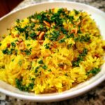 A close-up of vibrant yellow mediterranean rice topped generously with chopped fresh parsley and toasted pine nuts.