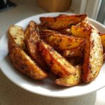 A close-up of golden brown, seasoned air fryer potato wedges piled high on a white plate.