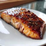 Close-up of a flaky, glazed air fryer salmon fillet with crispy edges served on a white plate.