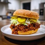 A close-up of amazing big mac sloppy joes piled high with meat sauce, shredded lettuce, and pickles on a sesame seed bun.