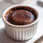 Close-up of a single serving of baked chocolate pudding with a slightly crusted top in a white fluted ramekin.