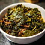Close-up of tender, dark green collard greens served in a white bowl with shredded smoked meat.